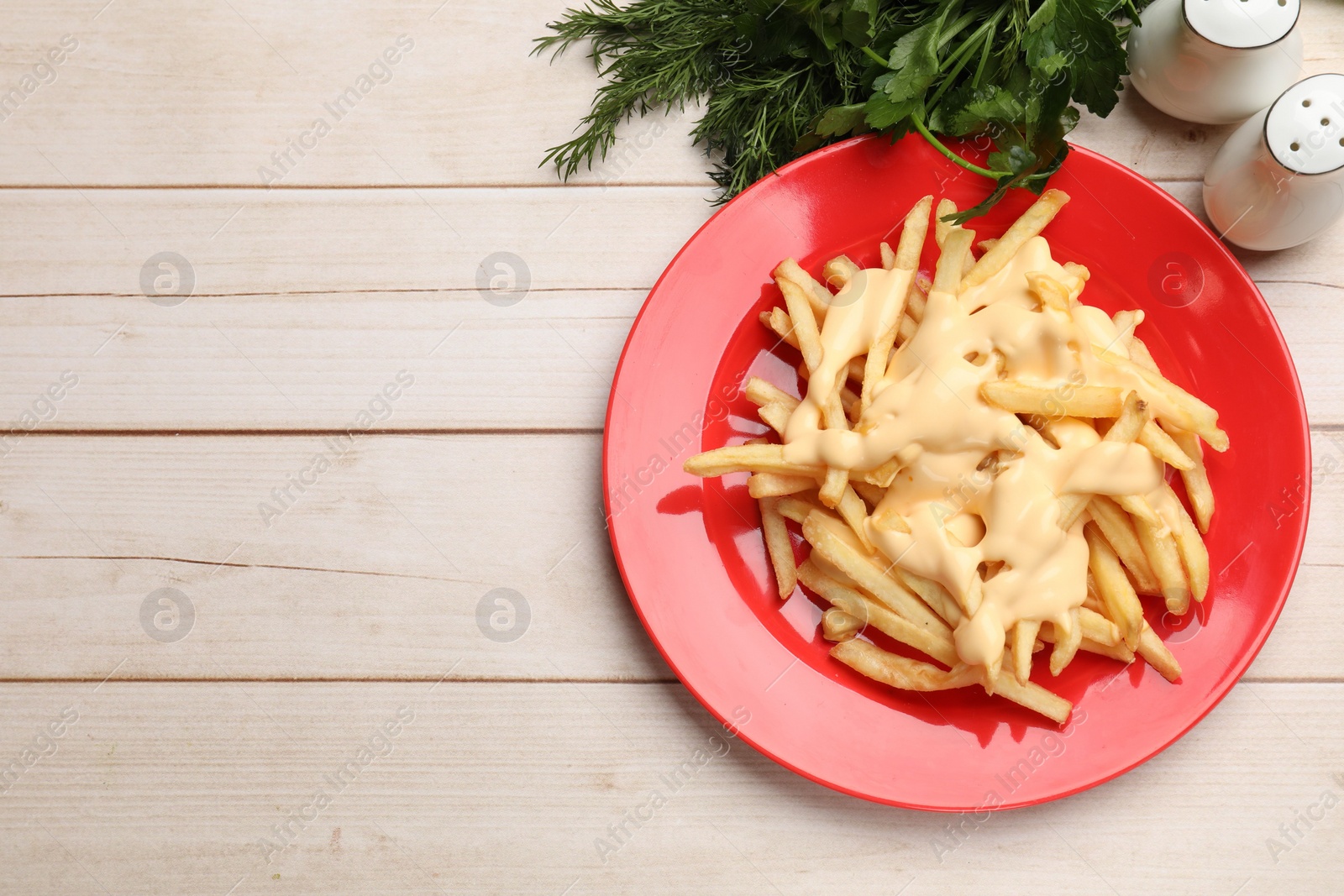 Photo of Delicious french fries with cheese sauce, greens and spice shakers on wooden table, flat lay. Space for text