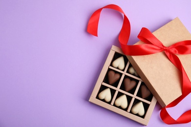 Photo of Tasty heart shaped chocolate candies on violet background, flat lay with space for text. Happy Valentine's day