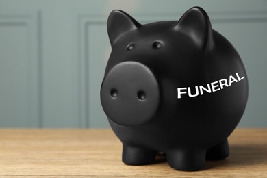 Money for funeral expenses. Black piggy bank on wooden table. Space for text