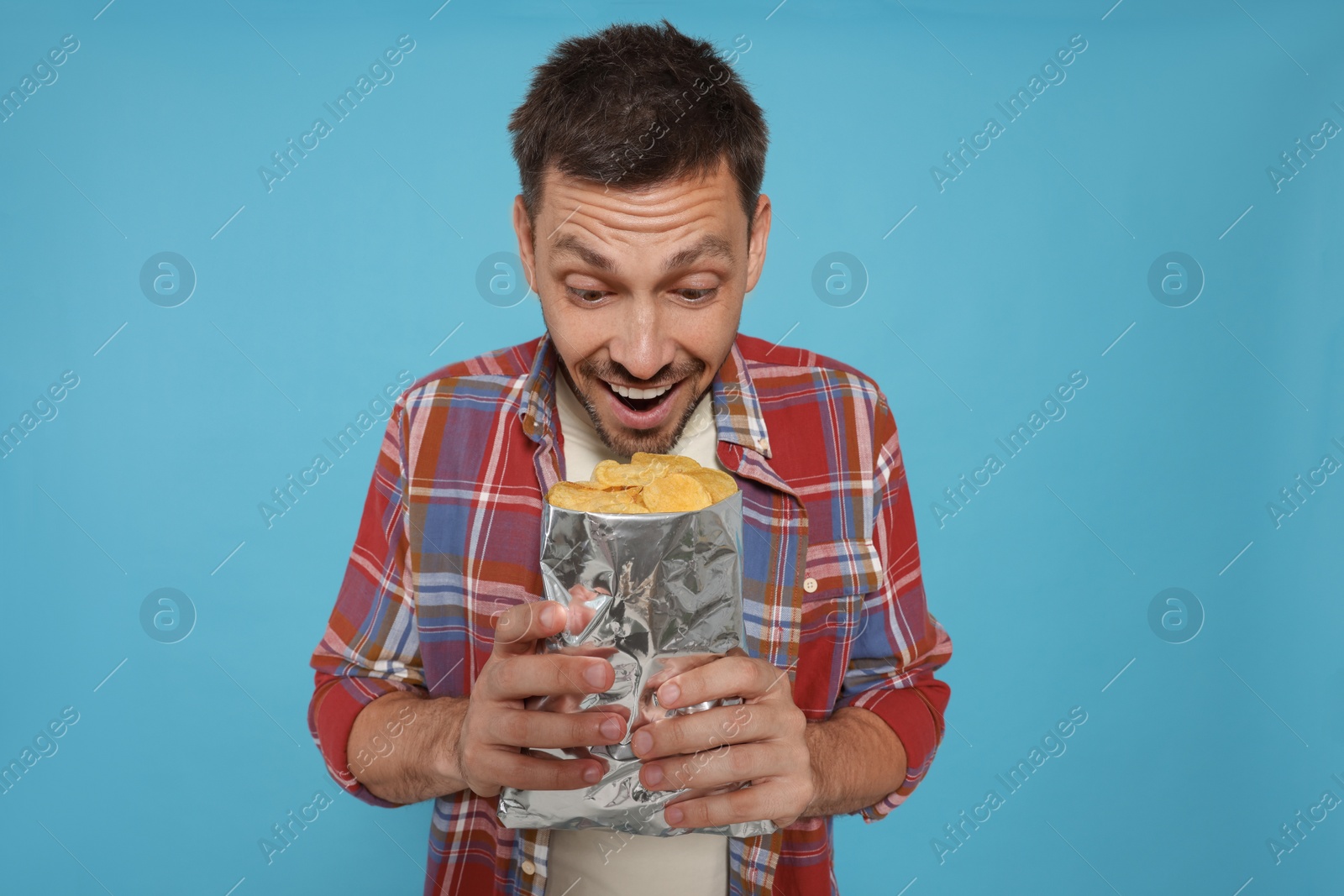 Photo of Excited man with potato chips on light blue background