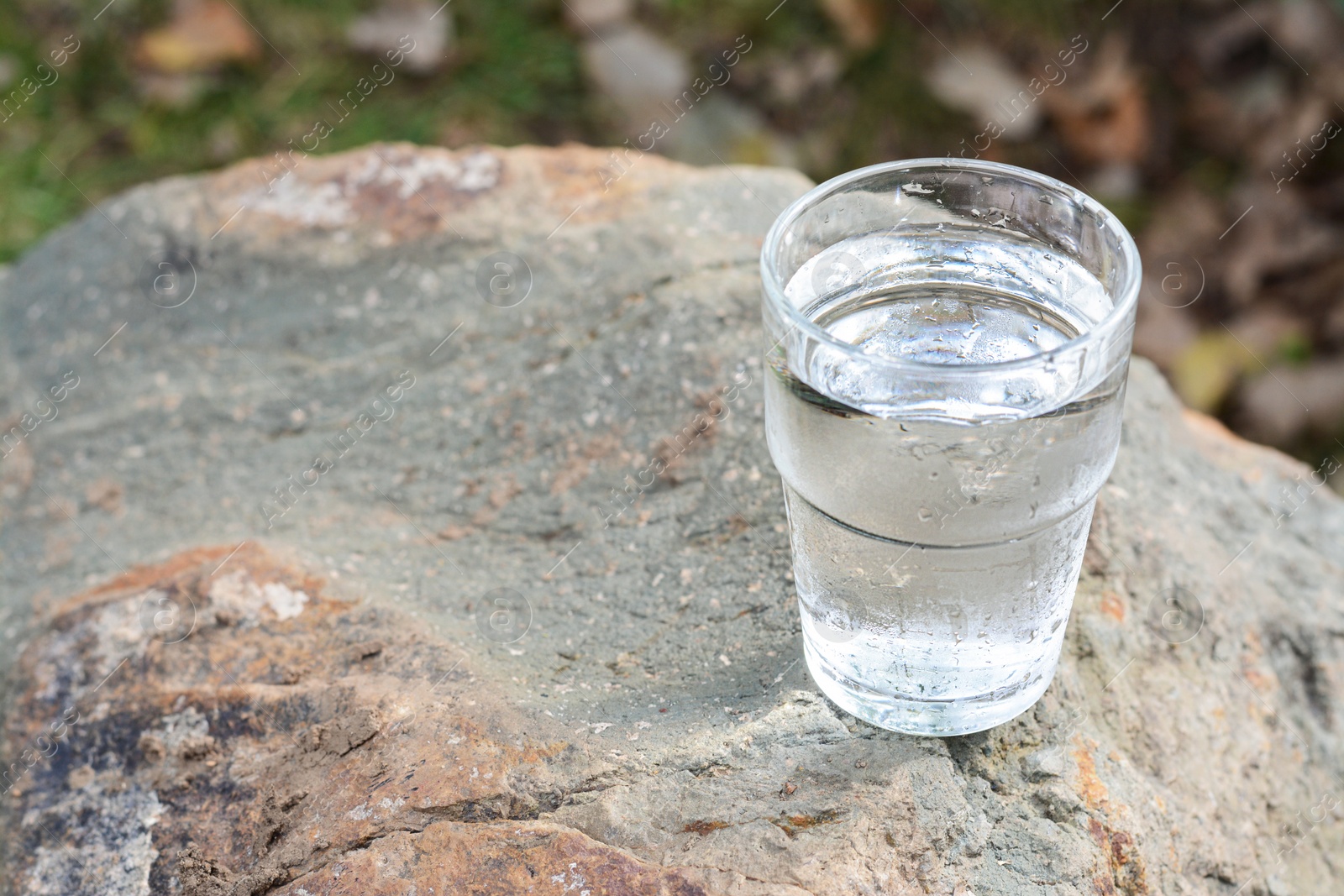 Photo of Glass of water on stone outdoors, space for text