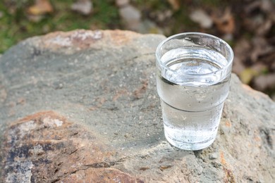 Glass of water on stone outdoors, space for text