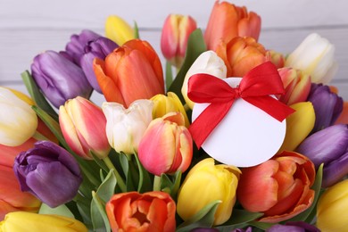 Bouquet of beautiful colorful tulips with blank card on white wooden background, closeup. Birthday celebration