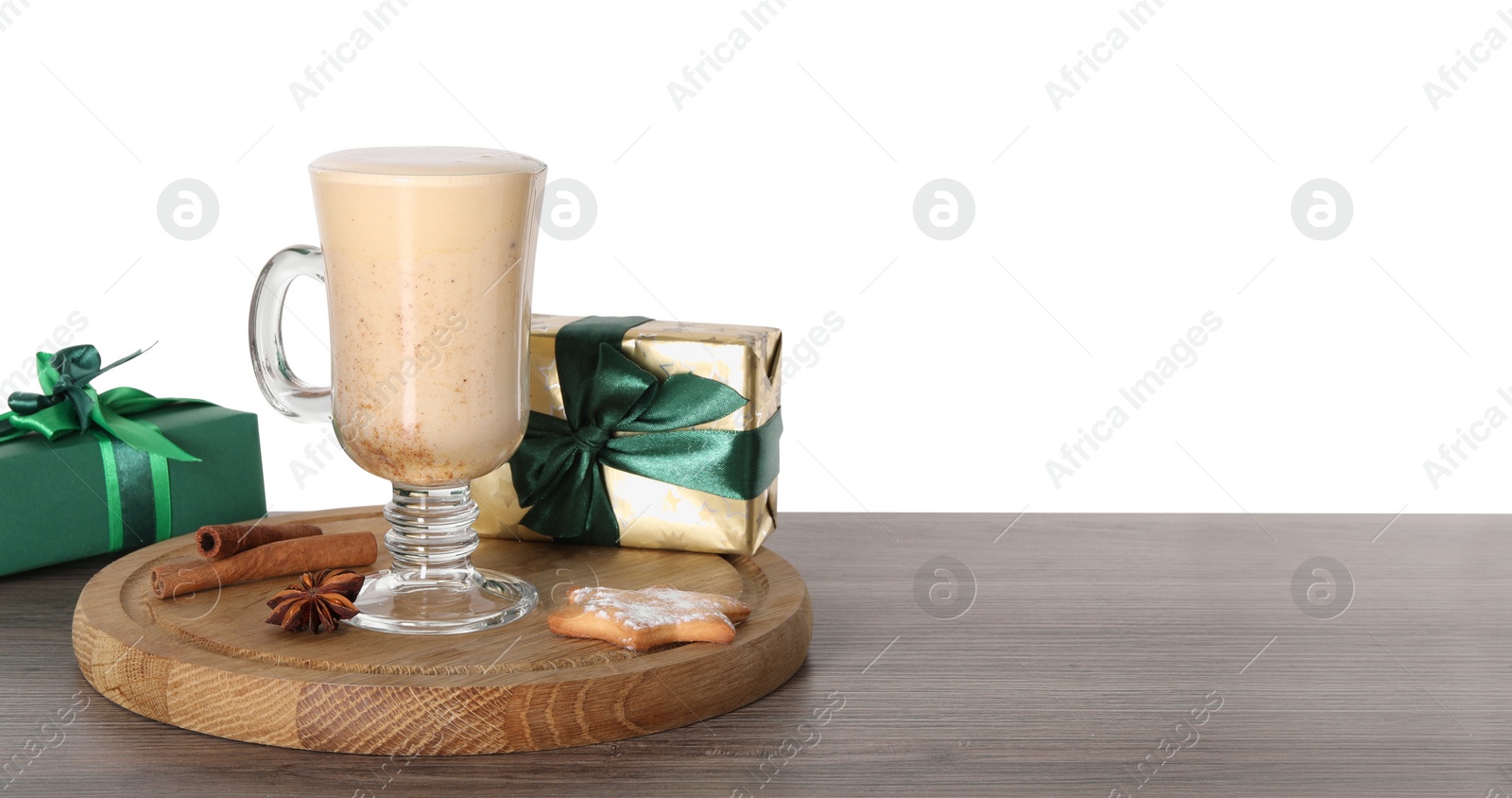 Photo of Delicious eggnog in glass, spices and gift boxes on wooden table against white background, space for text