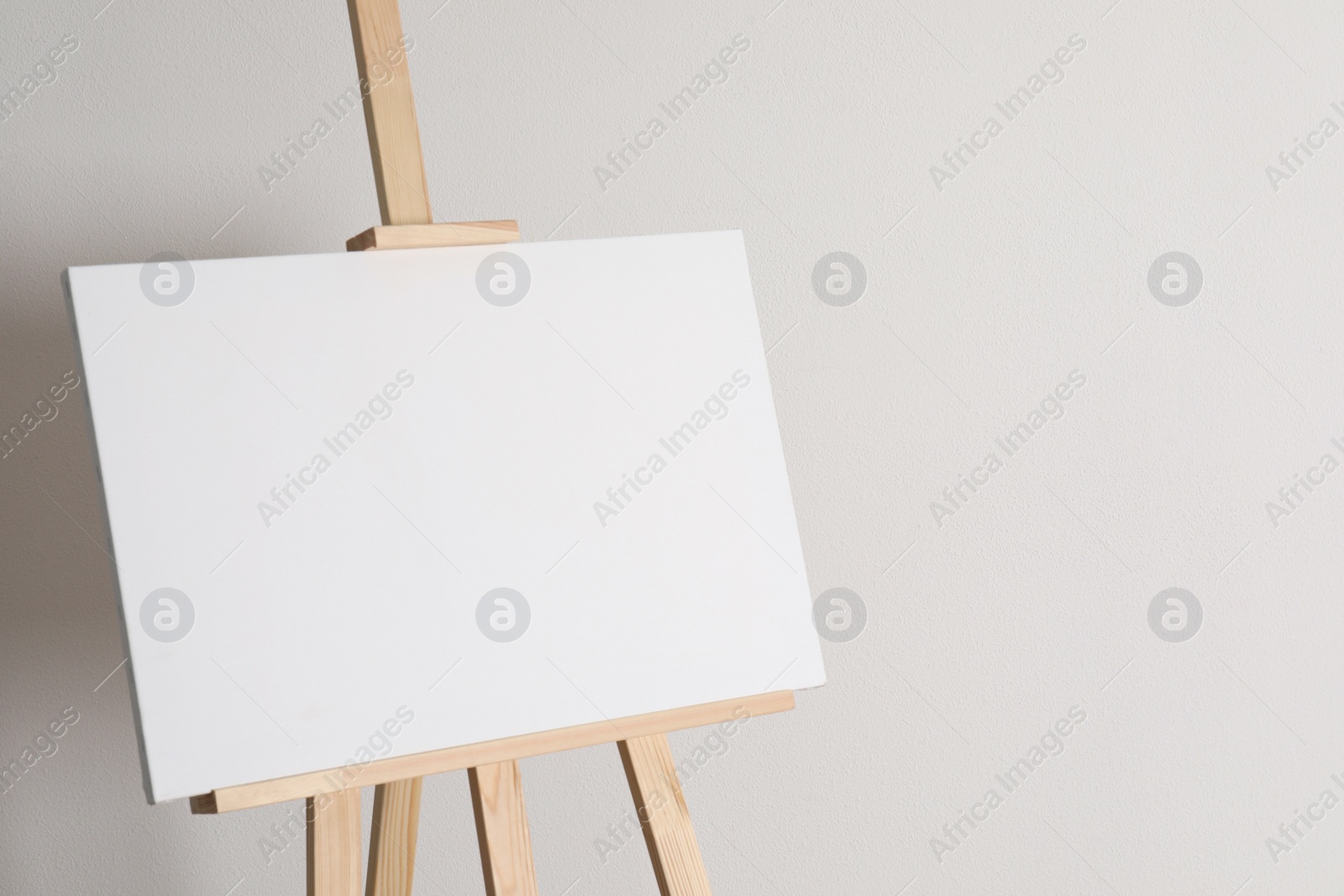 Photo of Wooden easel with blank canvas on light background. Space for text