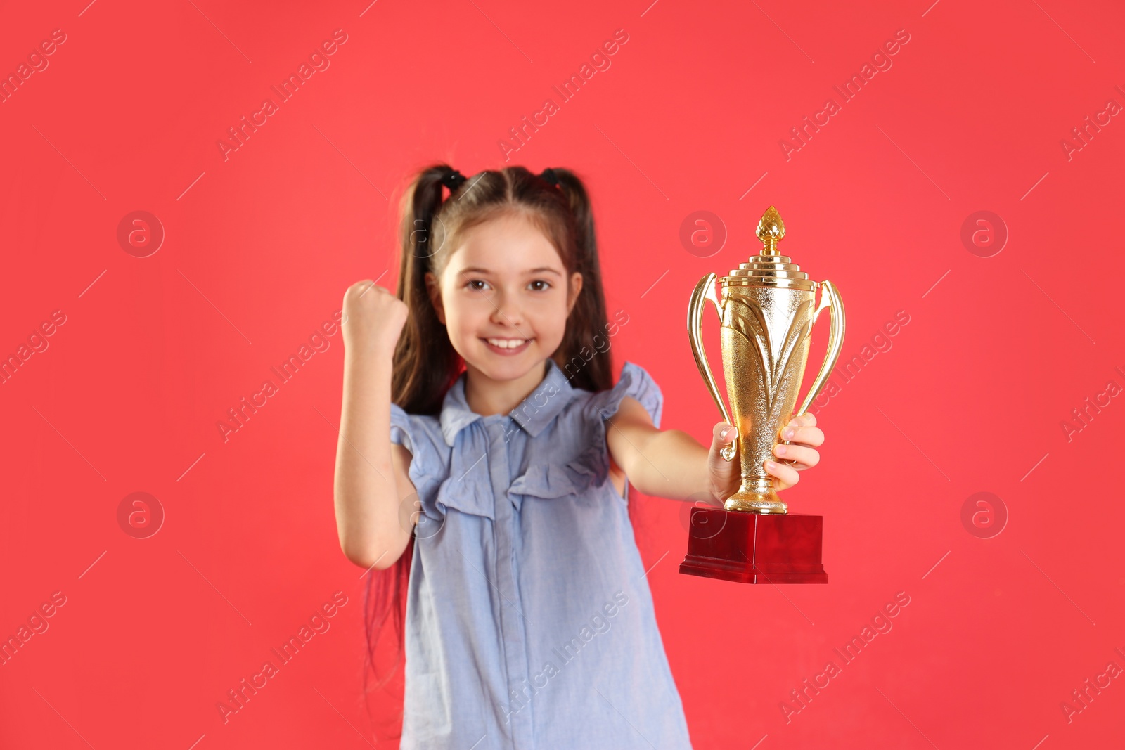 Photo of Happy girl with golden winning cup on red background