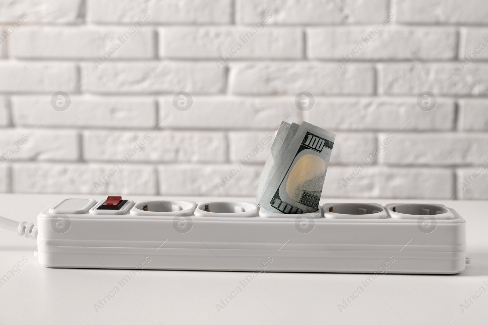 Photo of Extension board with rolled dollar banknotes on white table near brick wall