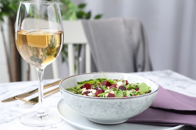 Delicious beet salad and glass of wine on white marble table indoors