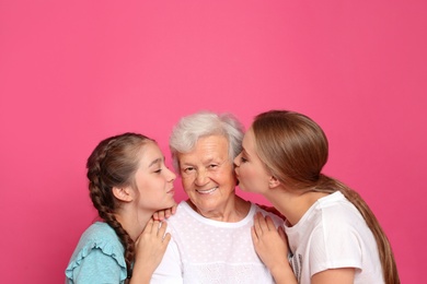 Happy sisters kissing their grandmother on pink background