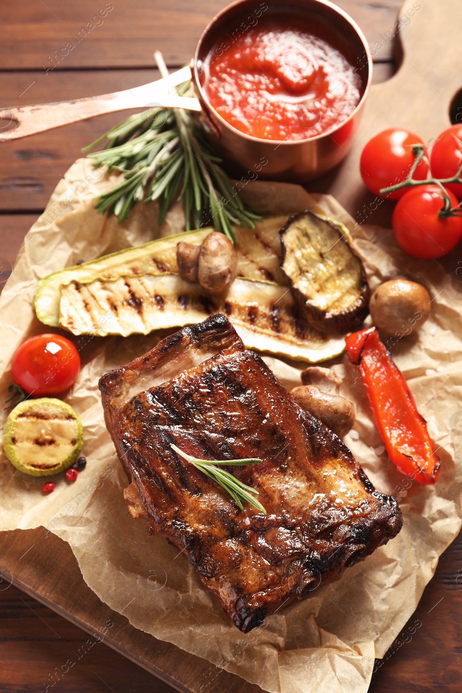 Photo of Delicious ribs served with vegetables for barbecue party on wooden table