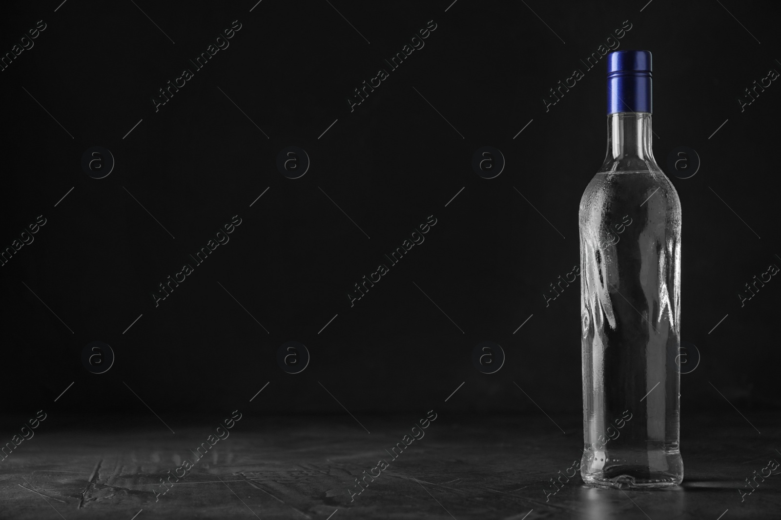 Photo of Bottle of vodka on grey table against black background. Space for text