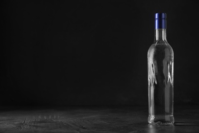 Photo of Bottle of vodka on grey table against black background. Space for text