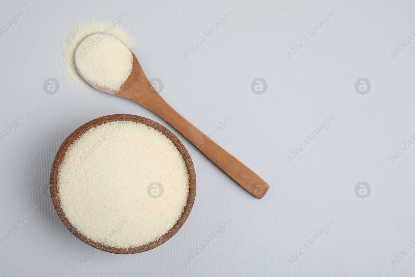 Photo of Wooden bowl and spoon with gelatin powder on light grey background, flat lay. Space for text