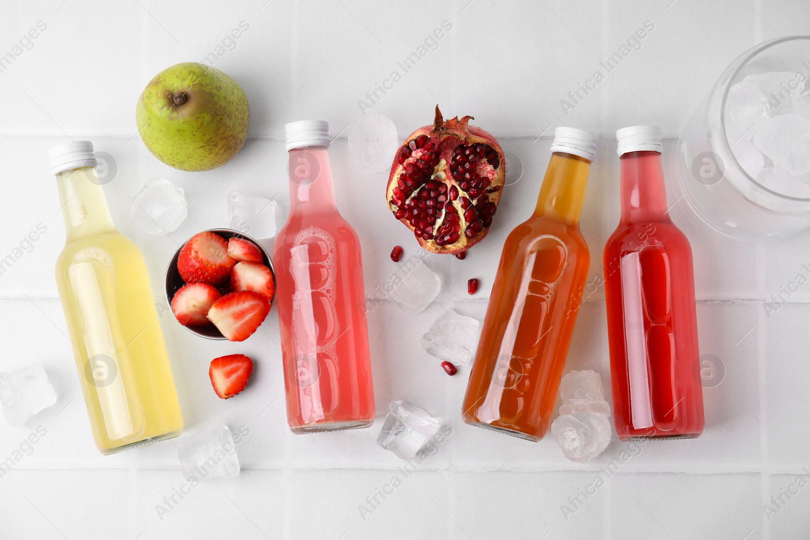 Photo of Tasty kombucha in glass bottles, fresh fruits and ice on white table, flat lay