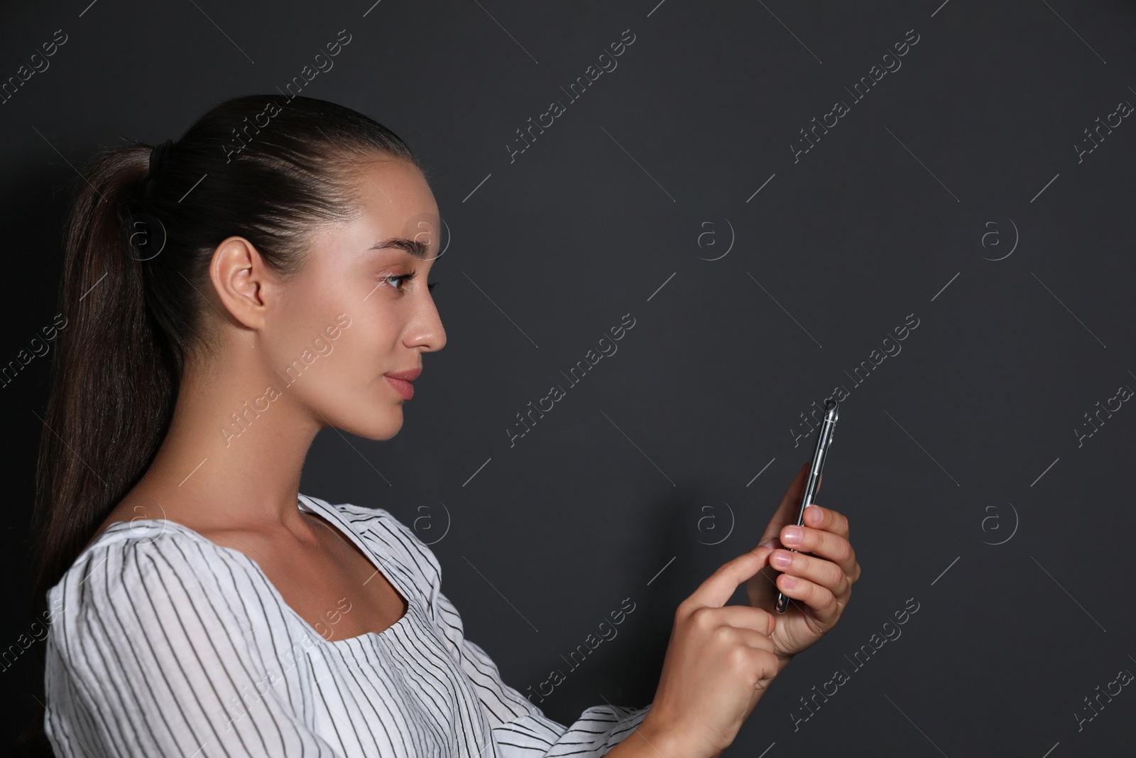 Photo of Young woman unlocking smartphone with facial scanner on black background. Biometric verification