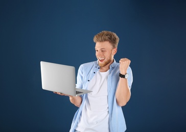 Emotional man with laptop on blue background