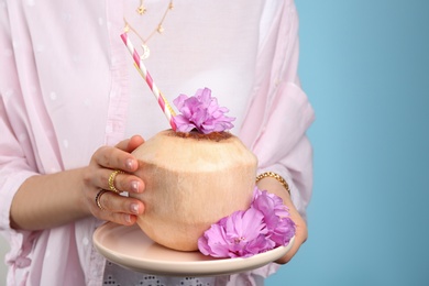 Photo of Woman holding fresh young coconut with straws on light blue background, closeup