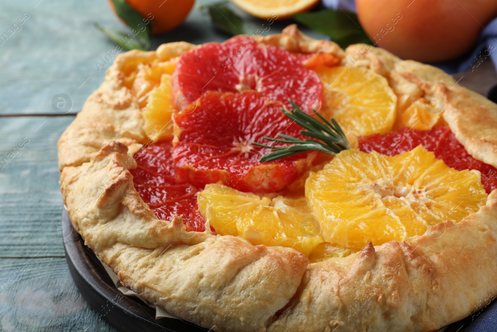 Photo of Delicious galette with citrus fruits and rosemary on blue wooden table, closeup