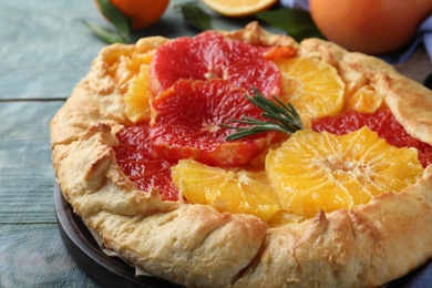 Photo of Delicious galette with citrus fruits and rosemary on blue wooden table, closeup