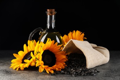 Sunflower cooking oil, seeds and beautiful flowers on grey table against black background