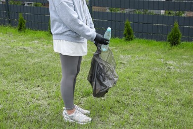 Photo of Woman with trash bag picking up plastic bottle outdoors, closeup. Recycling concept