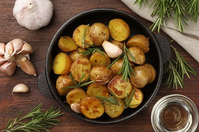 Delicious baked potatoes with rosemary and ingredients on wooden table, flat lay