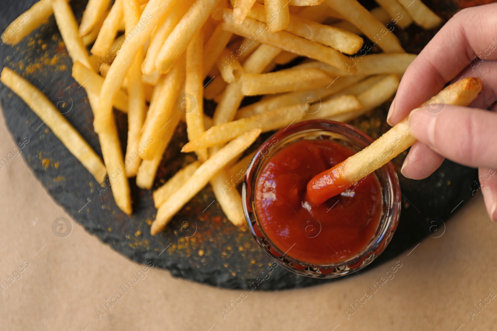 Photo of Woman dipping French fries into red sauce in cafe, closeup