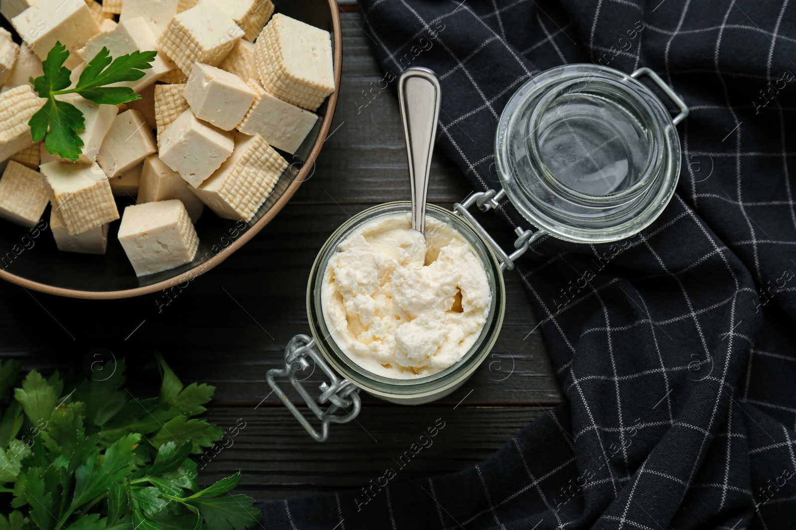 Photo of Delicious tofu cream cheese and parsley on black wooden table, flat lay