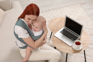 Photo of Mother holding her child in sling (baby carrier) on sofa indoors, above view