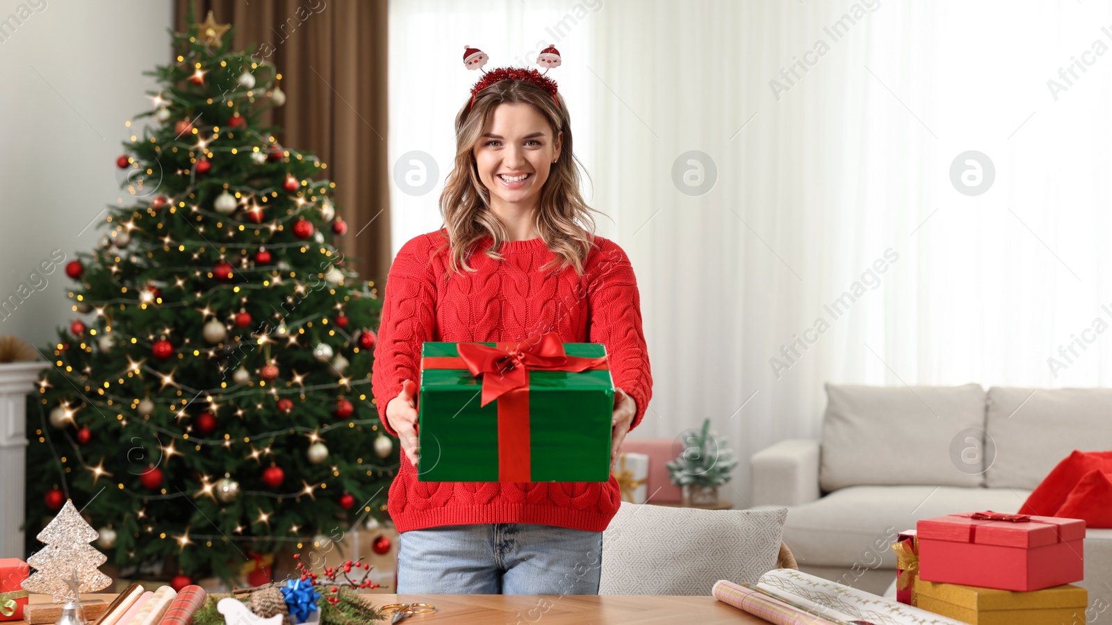 Photo of Young woman with beautifully wrapped Christmas gift at home