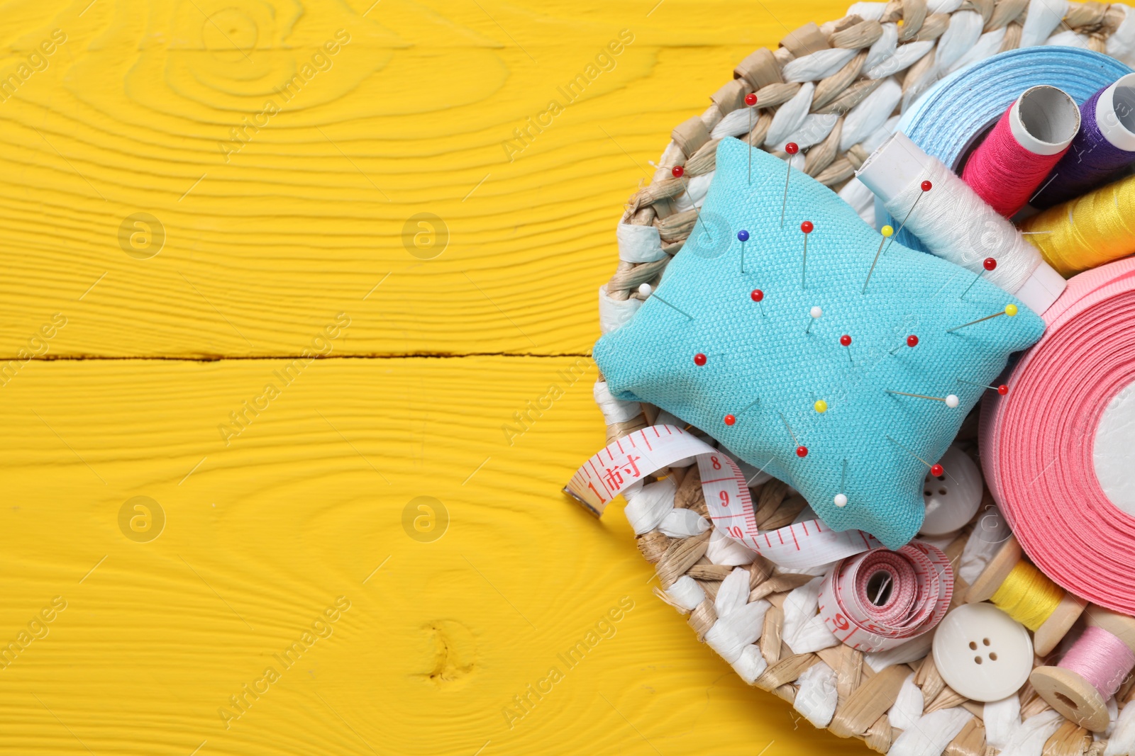 Photo of Light blue pincushion, pins and other sewing tools on yellow wooden table, top view. Space for text