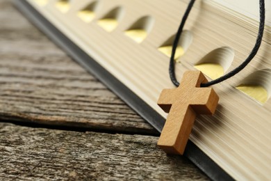 Photo of Christian cross and Bible on wooden table, closeup. Space for text