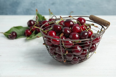 Metal basket with sweet red cherries on wooden table