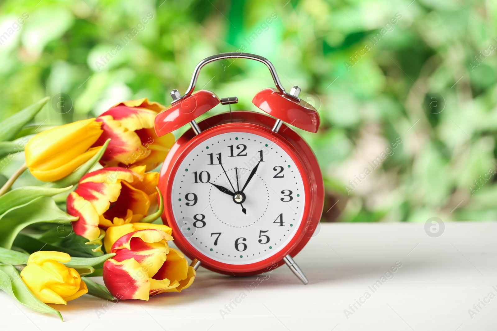 Photo of Alarm clock and spring flowers on white wooden table. Time change concept