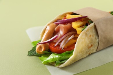 Delicious pita wrap with jamon, french fries and vegetables on light green background, closeup. Space for text