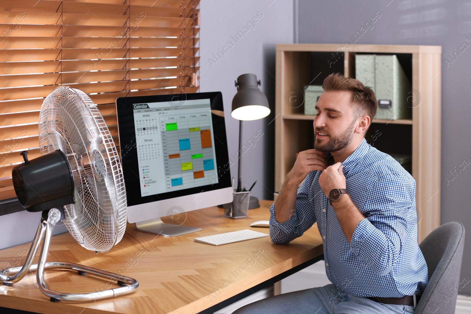 Photo of Man enjoying air flow from fan at workplace