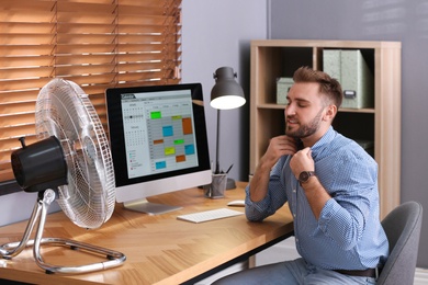 Man enjoying air flow from fan at workplace