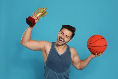 Photo of Portrait of happy young basketball player with gold trophy cup on blue background