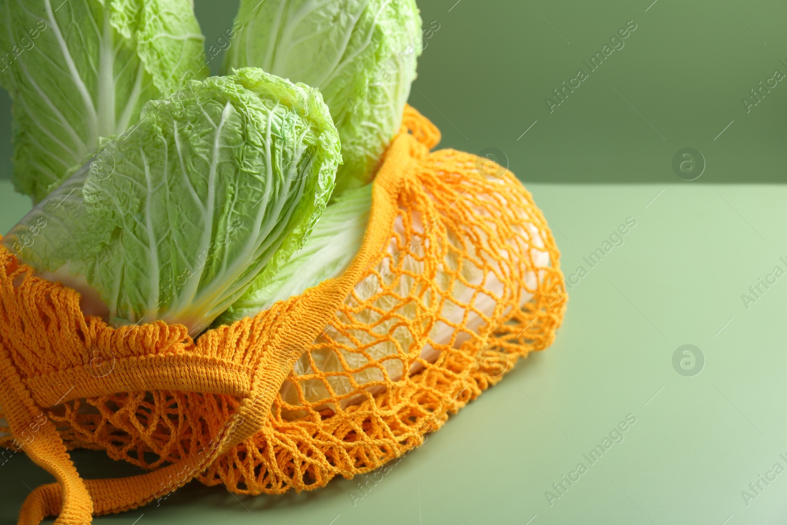 Photo of Fresh Chinese cabbages in string bag on green background, closeup. Space for text