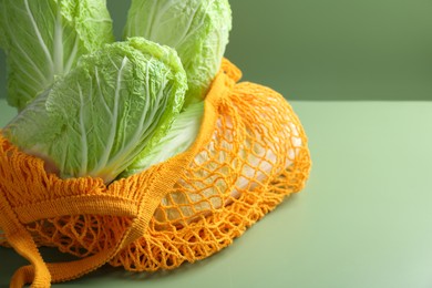 Photo of Fresh Chinese cabbages in string bag on green background, closeup. Space for text