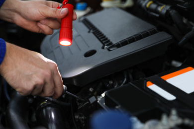 Photo of Mechanic with flashlight fixing car, closeup view