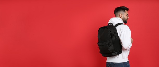 Photo of Young man with stylish backpack on red background, back view. Space for text