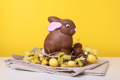 Beautiful composition with chocolate Easter bunny on white wooden table against yellow background