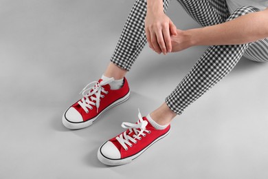 Photo of Woman wearing red classic old school sneakers on light grey background, closeup