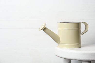 Beige metal watering can on table against white wooden background, space for text