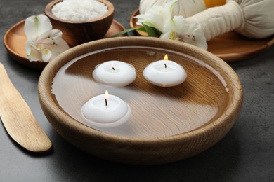 Photo of Spa composition with burning candles in bowl with water on grey table