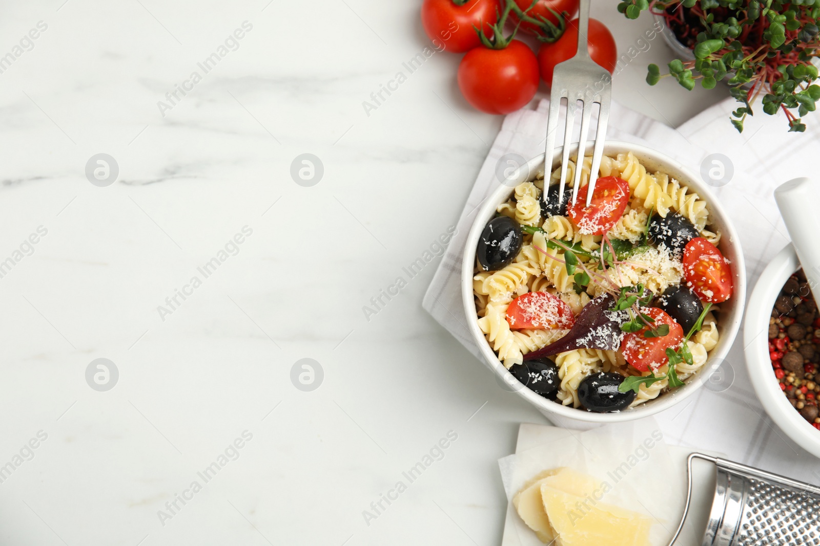 Photo of Bowl of delicious pasta with tomatoes, olives and cheese on white table, flat lay. Space for text