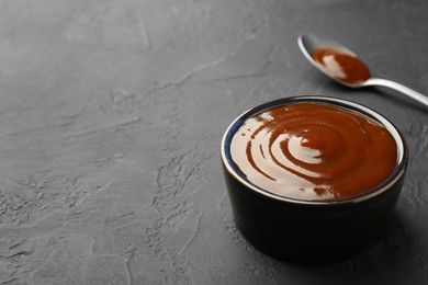 Photo of Tasty barbeque sauce in bowl on dark textured table, closeup. Space for text