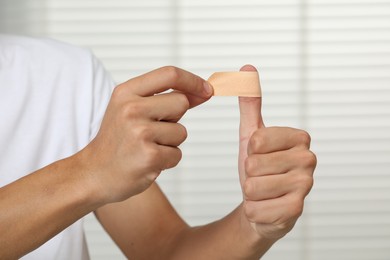 Man putting sticking plaster onto thumb indoors, closeup