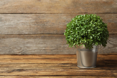 Photo of Artificial plant in metal flower pot on wooden table. Space for text